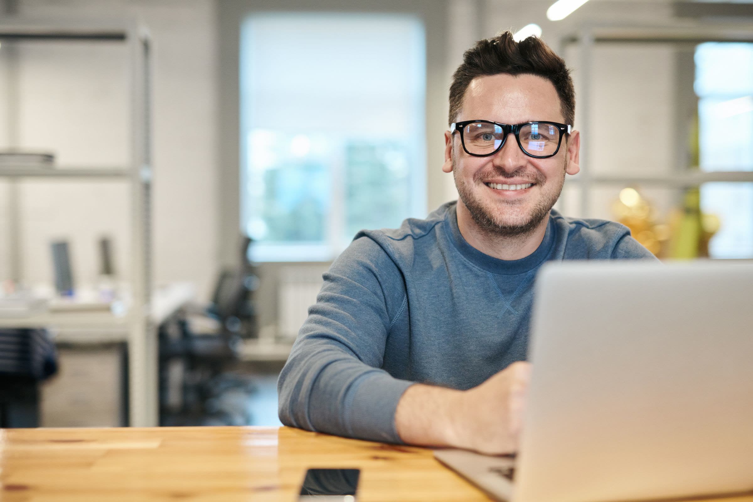 A smiling business owner with glasses at his laptop